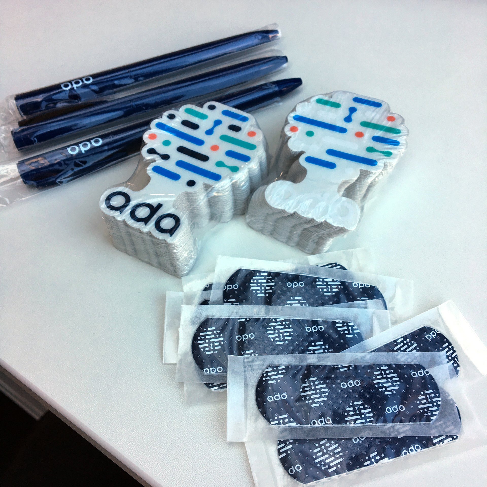 Promotional swag detail — navy Ada pens, illustrated brand-system stickers, and branded band-aids in their packaging