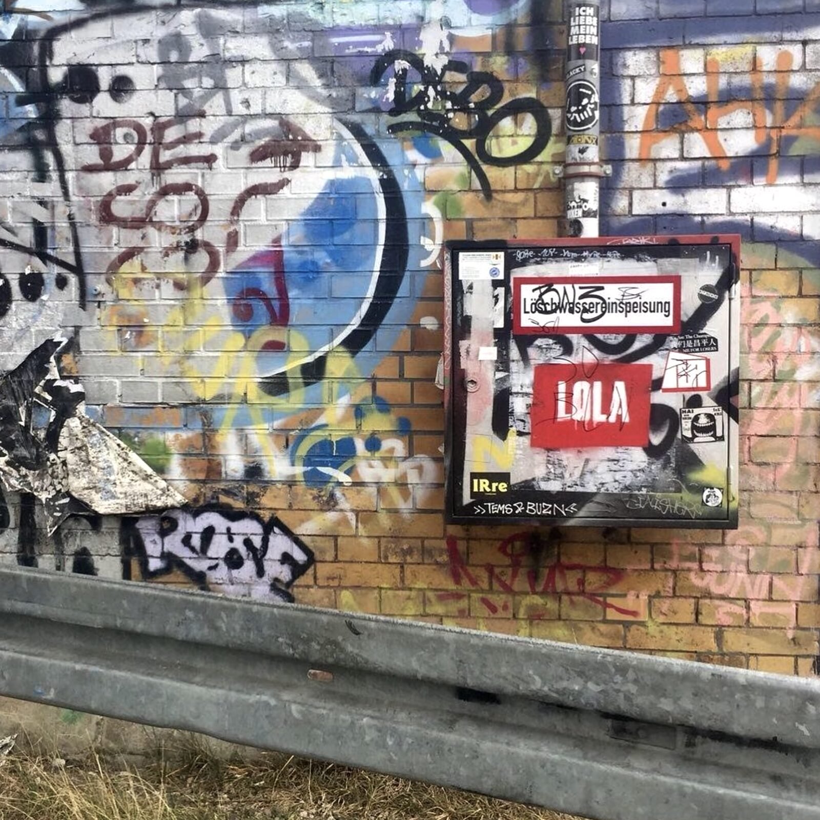 LOLA sticker on a graffitied utility box in Berlin — bold red square holding its own in the street layer